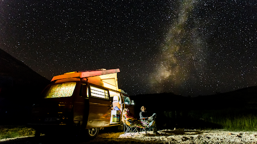 Couple in front of their van conversion looking at the stars reading a vanlife guide.